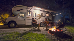 A family sits around a campfire outside their RV.